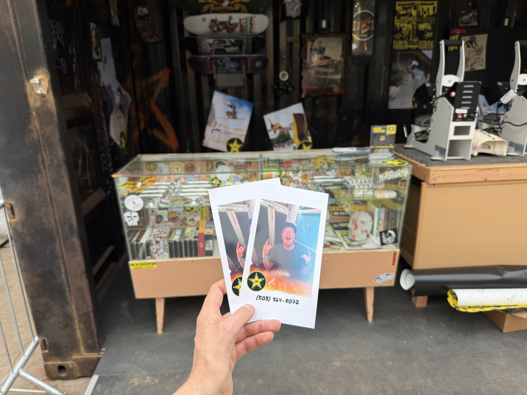 A hand holding two printed Rockstar booth portraits in front of the installation.